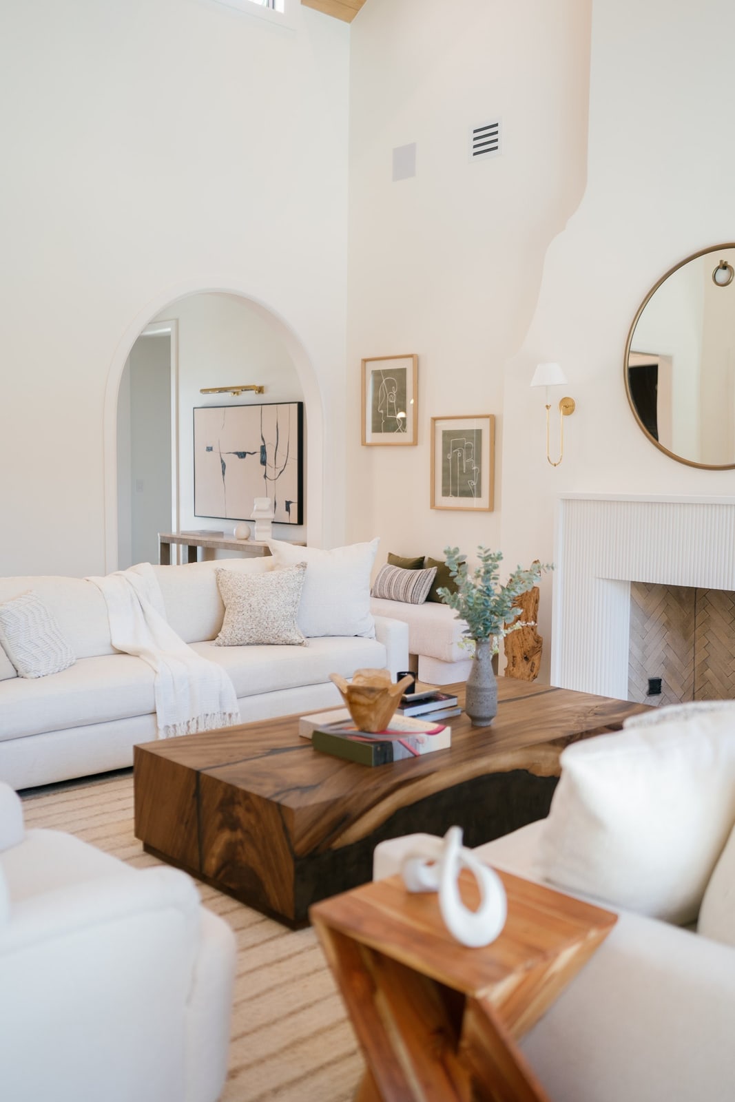 White living room with an arched niche, fireplace, wood slab coffee table and cream sofas.