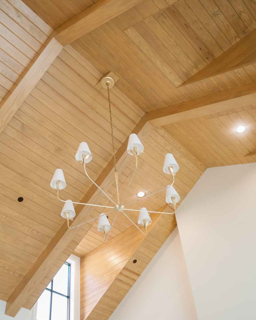 Vaulted white-oak ceiling with exposed beams and a white branch chandelier.
