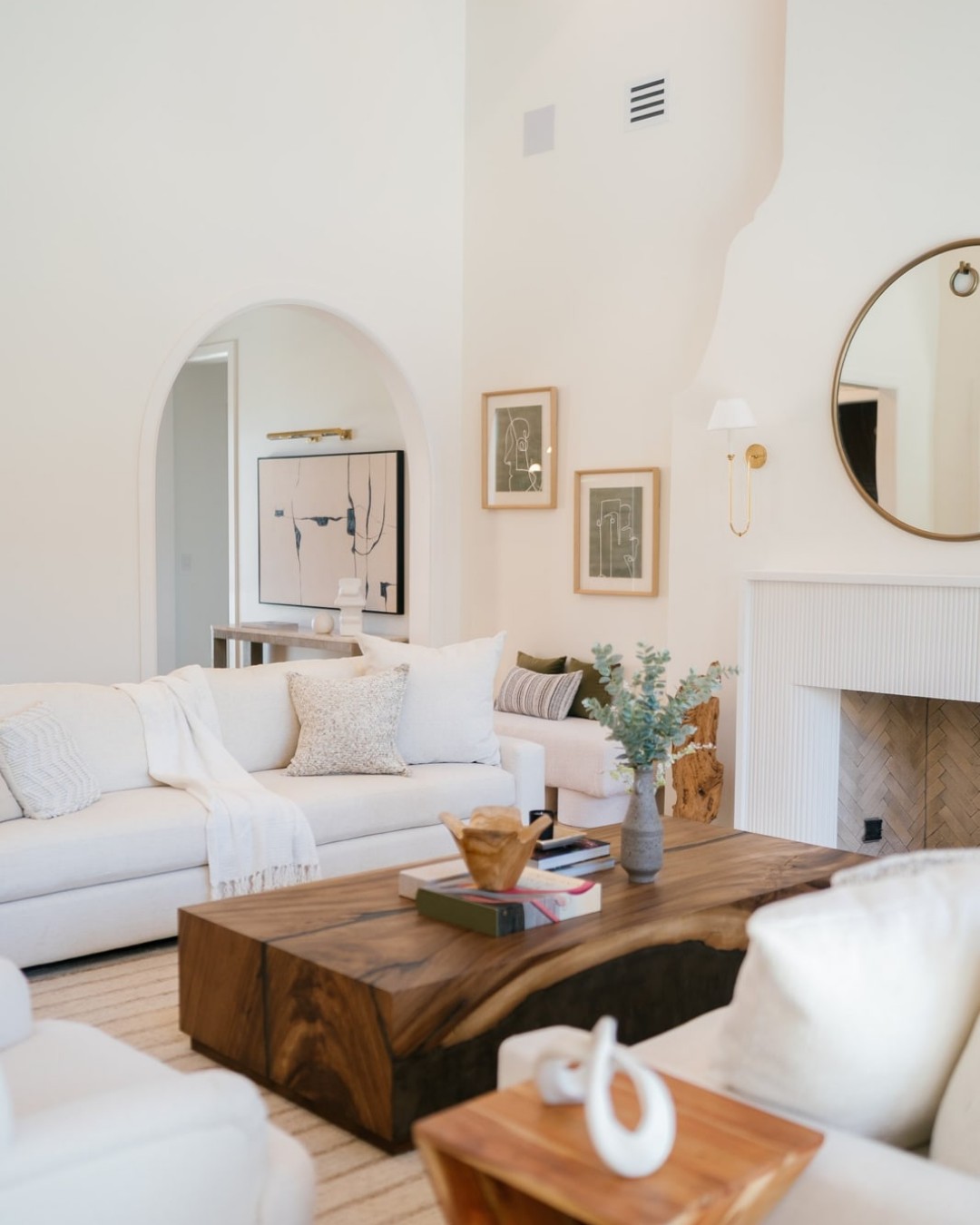 White living room with an arched niche, fireplace, wood slab coffee table and cream sofas.