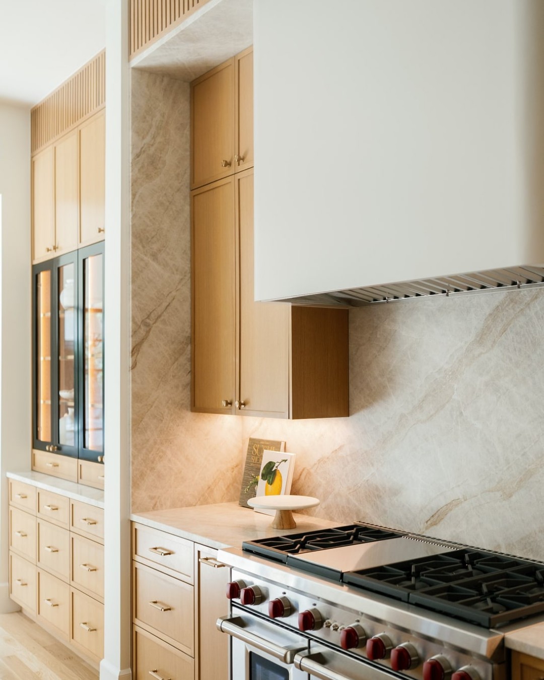 Professional gas range set into a marble slab backsplash with a white plaster hood.