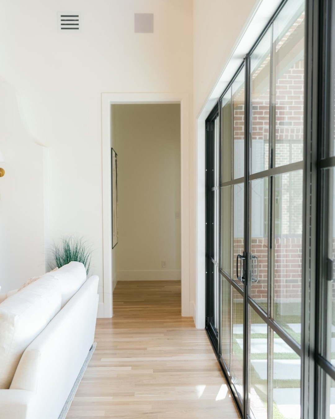 Hallway with oak floors lined by floor-to-ceiling black steel windows.