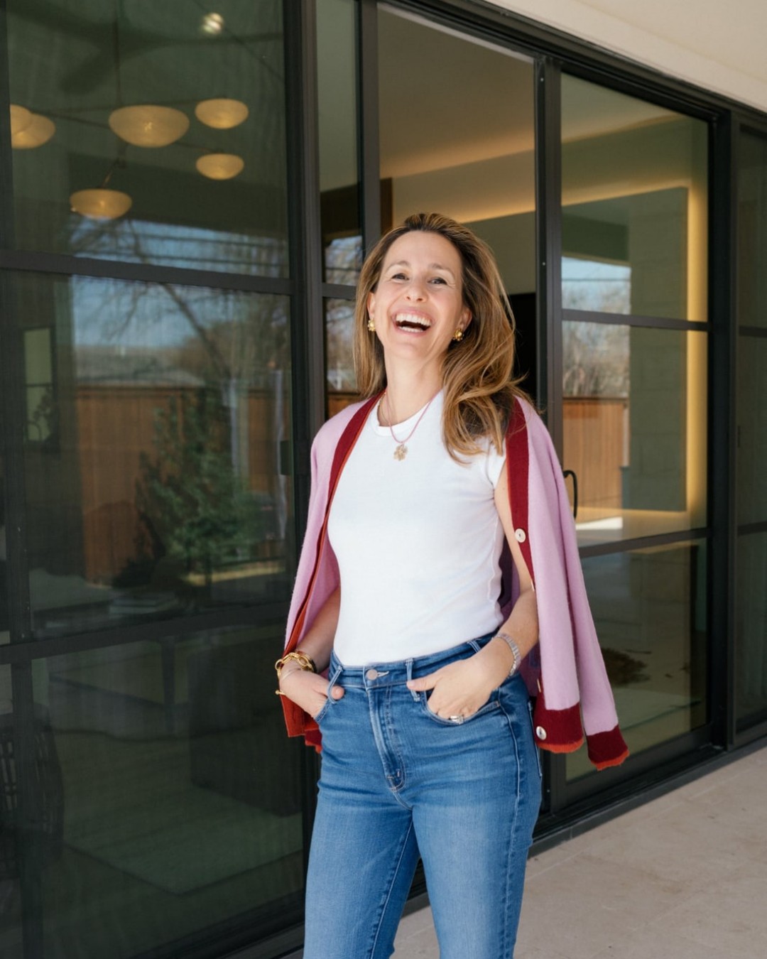Smiling woman in jeans standing in front of black-framed glass doors.